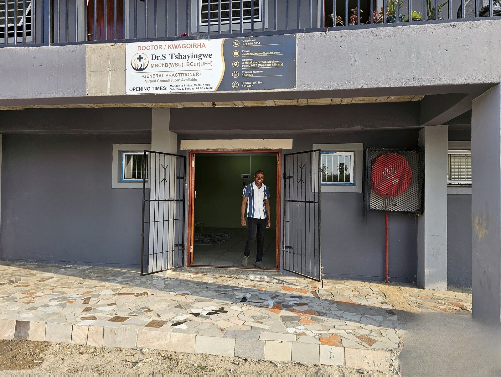 Dr Sivuyile Tshayingwe standing at the entrance of the practice at 3 Matakata Street, Mbekweni, under the practice sign